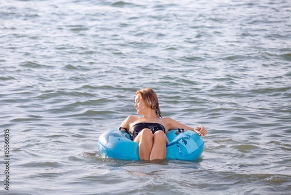 Fototapeta A young girl swims in the sea with an inflatable circle