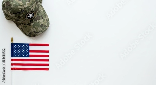 Obraz A flat lay composition of a military-style veteran cap placed beside a carefully laid small U.S. flag on a white background.