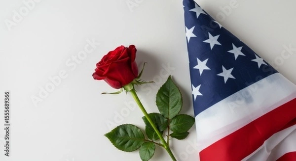 Obraz A red rose placed gently beside a folded U.S. flag, photographed on an isolated white background.