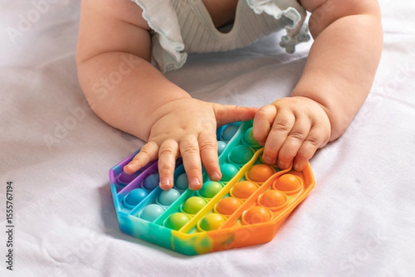 Fototapeta Newborn baby lies on his stomach playing trendy flexible silicone colorful toy Pop it