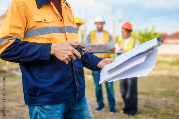 Fototapeta At a table on a construction site, an elderly male safety expert, a middle-aged man, and two young Asian women gather around a laptop to actively document, coordinate plans, and execute projects