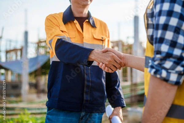 Fototapeta An elderly engineer and a middle-aged man shake hands at a construction site, symbolizing mutual respect, collaboration,professional commitment in engineering and construction project environments