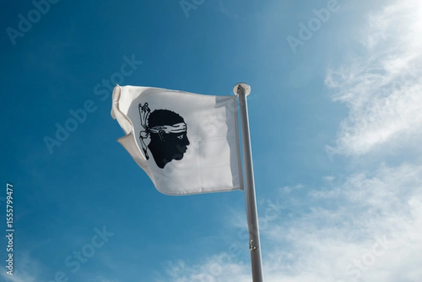 Fototapeta The Moors head of the Corsican flag fluttering in the wind on a flagpole against a deep blue sky