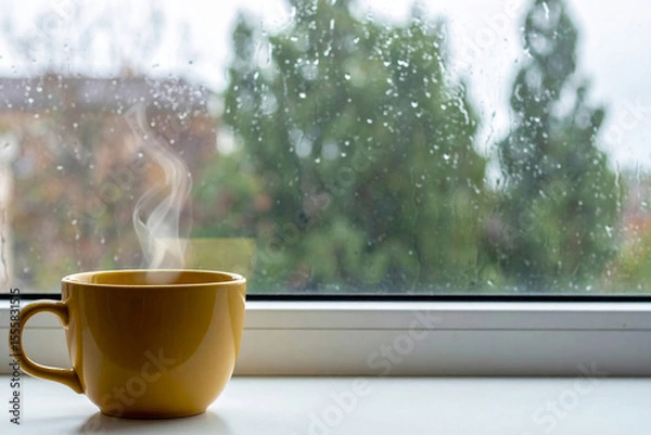 Fototapeta Yellow coffee cup with smoke floating near the window on a rainy day