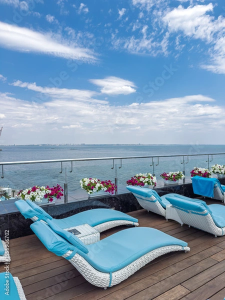 Obraz Relaxation area with modern white and blue chaise longues on a terrace with a panoramic sea view. Perfect summer background for travel and leisure, with no people.
