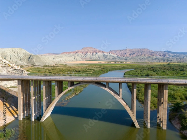 Fototapeta Nallihan Bird Sanctuary (Nallihan Kus Cenneti) Majestic arch bridge spans a serene river landscape. An expansive view of a large, concrete arch bridge gracefully crossing a calm river. ANKARA TURKIYE 