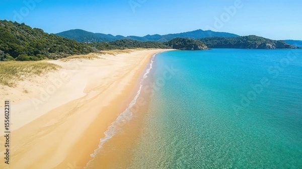 Fototapeta Aerial view of a sandy beach with clear turquoise water and green hills in the distance on a sunny day
