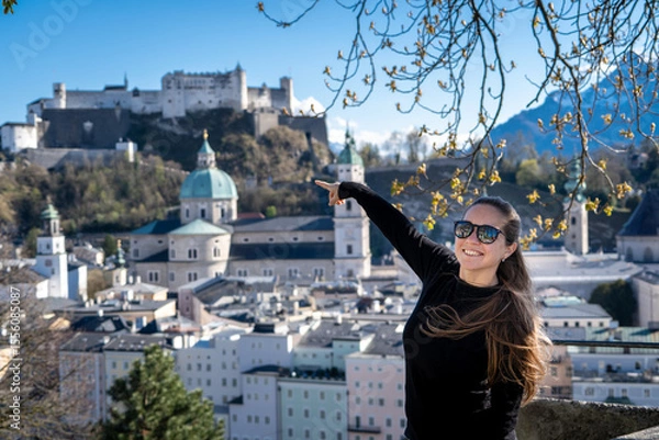Obraz Mujer turista feliz explorando la ciudad de Salzburgo, apuntando al castillo con el dedo desde un mirador en altura