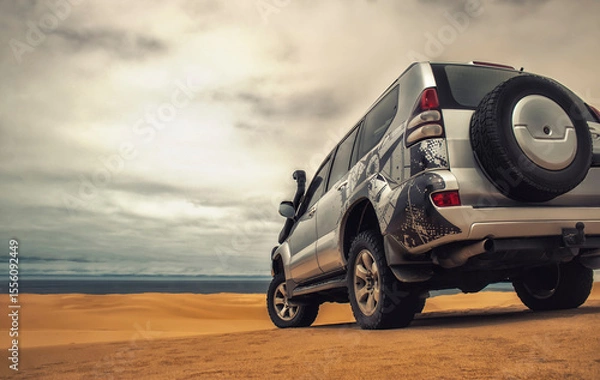 Fototapeta A powerful gray 4x4 SUV stands alone in the vast sandy terrain of the Namib Desert, ready for off-road travel, exploration, and endurance across one of Africa’s wildest landscapes. 