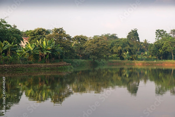 Obraz Tranquil Tropical Lakeside Scene with Lush Greenery Reflected in Clear Waters