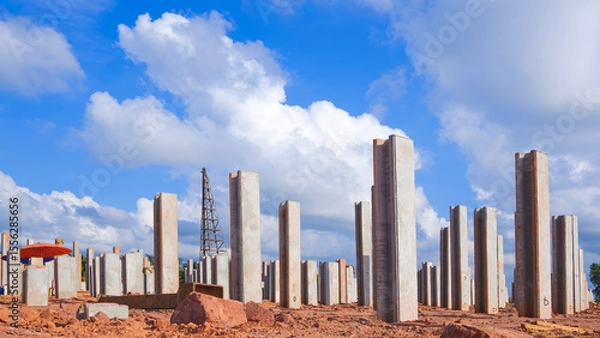 Fototapeta Many precast concrete piles foundation structure on the ground with pile driver machine in industrial factory building construction site against clouds on blue sky background