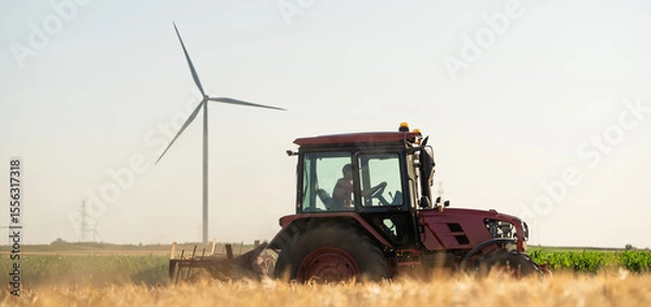Fototapeta Agricultural tractor is working on the field with wind turbines