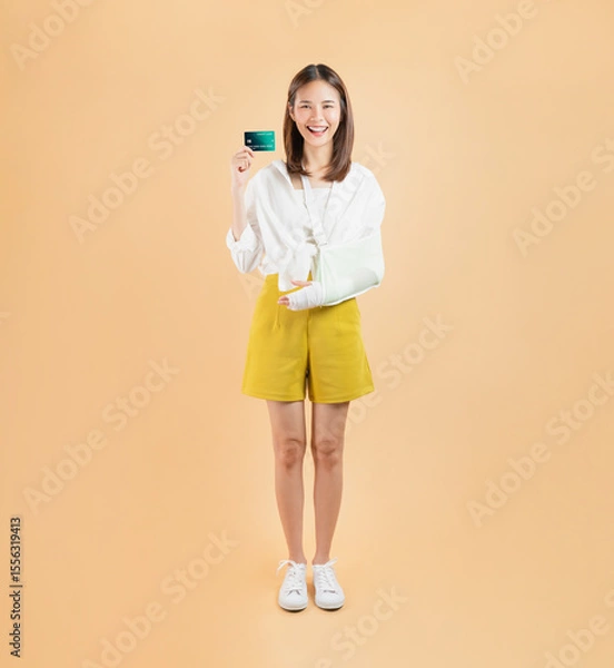Fototapeta Asian young woman with a broken arm wrapped in bandages, representing the concept of purchasing accident insurance to protect against unexpected events, paid with a credit card.