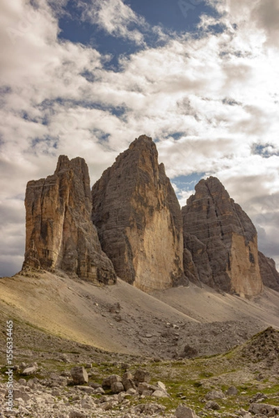 Obraz Iconic mountain peaks known as the Tre Cime di Lavaredo rise above a rocky valley in the Italian Alps. Dramatic clouds and rugged terrain evoke a sense of wilderness and grandeur.
