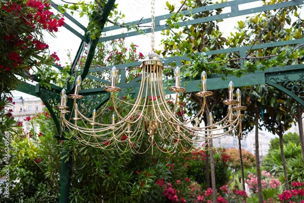 Fototapeta A decorative arch decorated with lush greenery and round illuminated chandeliers.