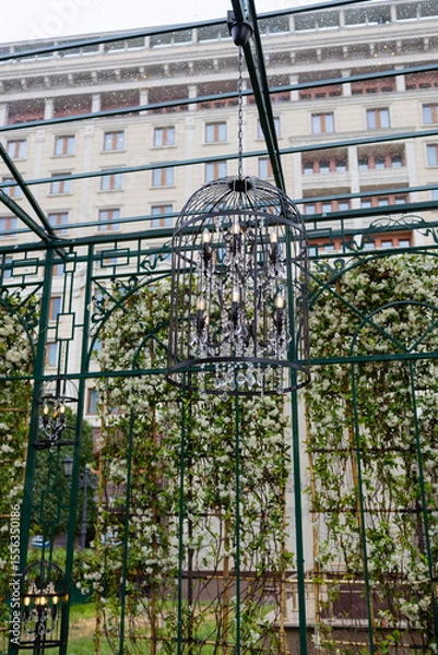 Fototapeta A decorative arch decorated with lush greenery and round illuminated chandeliers.