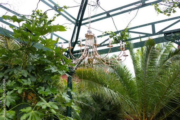 Fototapeta A decorative arch decorated with lush greenery and round illuminated chandeliers.