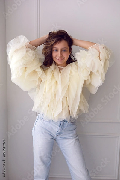 Obraz A portrait of a fashionable teenage girl in blouse and sneakers dancing in a studio on a light wall in a room. light from the window