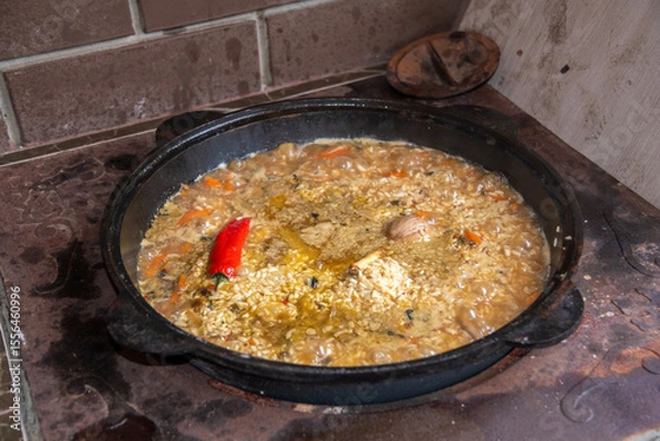 Fototapeta Traditional dish of pilaf is simmering in a cauldron on a wood burning stove, featuring rice, carrots, spices, and a touch of hot pepper for an authentic culinary experience