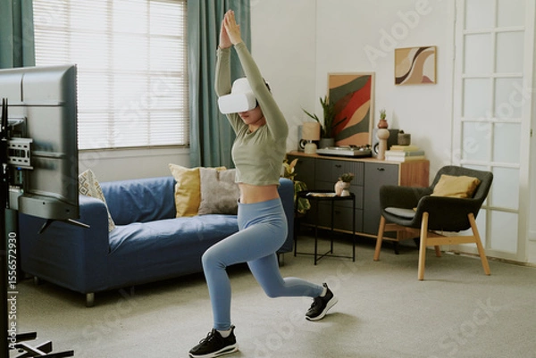 Obraz Teenage Caucasian girl exercising with VR headset in living room, performing lunge in front of television, engaging in interactive fitness activity, spending leisure time at home