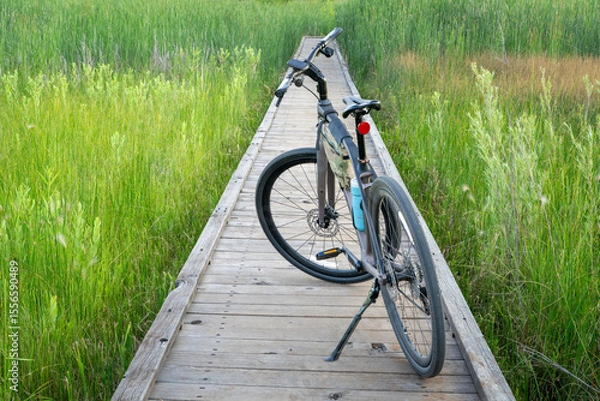 Obraz hybrid bike with kickstand, frame bag and cycling computer on a boardwalk across wetland in summer scenery
