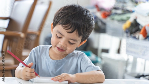 Fototapeta A cheerful young boy enjoying his drawing activity, showcasing concentration and joy during early education at home.