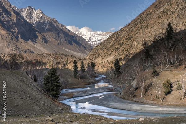 Obraz Mountain Stream Winding Through Bare Trees and Snowy Peaks