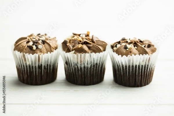 Fototapeta Chocolate cupcakes are showing in flat design on white table with liners, frosting and toppings