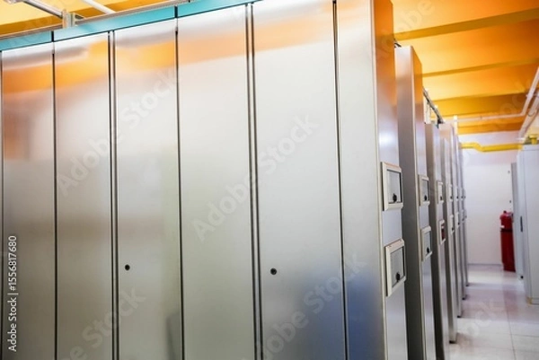 Fototapeta Row of tall grey cabinets is lining narrow corridor flat, with yellow ducts and red extinguisher