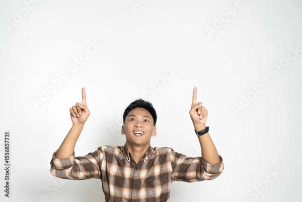 Fototapeta Cheerful young man enthusiastically pointing upwards, showcasing excitement and joy. Ideal image for concepts such as encouragement, positivity, or enthusiasm.