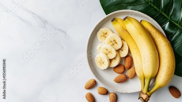 Fototapeta White plate with a bunch of bananas and sliced bananas on it. the bananas are yellow with brown spots and appear to be ripe and ready to eat. there are also a few almonds scattered around the plate.