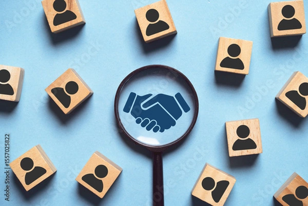 Fototapeta This image highlights the importance of collaboration and partnership, featuring a handshake within a magnifying glass surrounded by blocks symbolizing people.