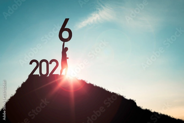 Fototapeta Silhouett  person triumphantly holds up the number 6 on a hill, symbolizing achievement and new beginnings. The sun setting in the background adds a sense of hope and potential for the year 2026.