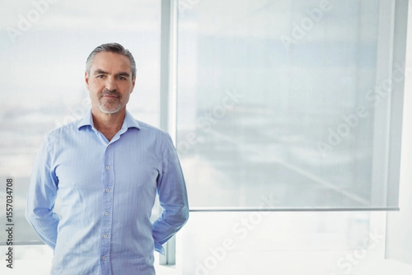 Fototapeta Businessman standing with hands behind back by office window roller blind diffusing cityscape light