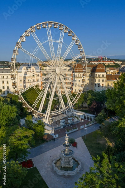Fototapeta The famous ferris wheel in Budapest included the Danubius fountain. Lush green trees at spring time. Located the Erzsebet park in downtown in capital of Hungary.