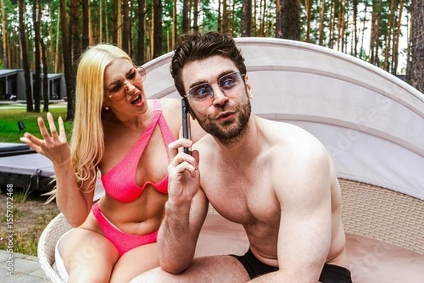 Fototapeta Bearded man talking on smartphone while his girlfriend swearing at him, resting on the sunbed. Summer vacation, relationship, lifestyle concept