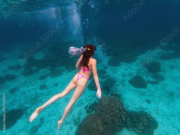 Fototapeta A swimmer explores a vibrant coral reef while scuba divers observe nearby. Sunlight filters through the clear water, illuminating this underwater paradise filled with marine life.