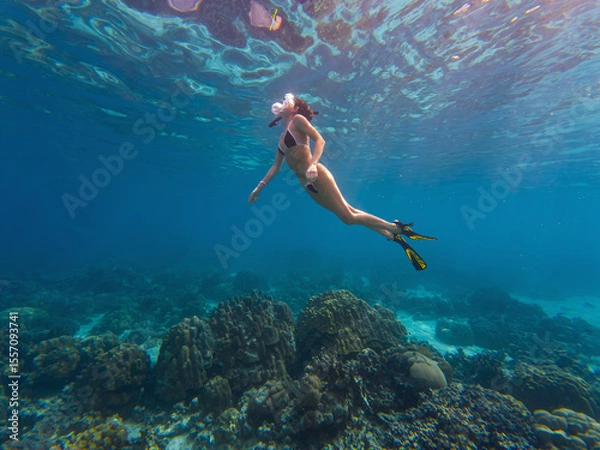 Fototapeta A person enjoys snorkeling in clear turquoise waters above a colorful coral reef, exploring marine life beneath the surface. The sunlight creates a shimmering effect on the water.