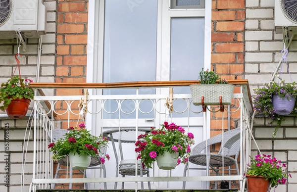 Fototapeta Balcony of an apartment building with a table and chairs decorated with flowers in pots and boxes.