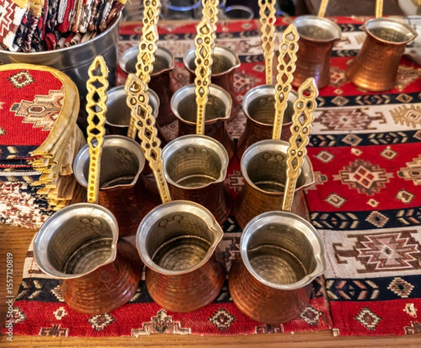 Obraz Preparation for brewing strong Turkish coffee. A group of vintage-style hammered copper pots (cezve) on a traditional textile background.Equipment for brewing traditional hot coffee.