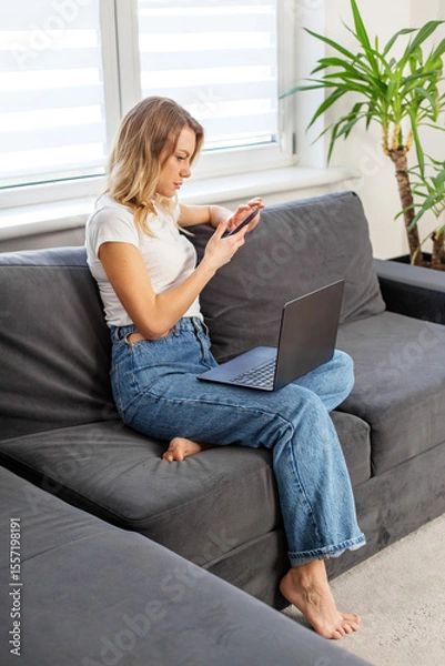 Fototapeta Remote worker using phone and laptop at home