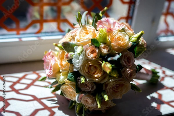 Fototapeta Flower bouquet by window. A vibrant bouquet of roses and other flowers rests elegantly on a table near a sunlit window.