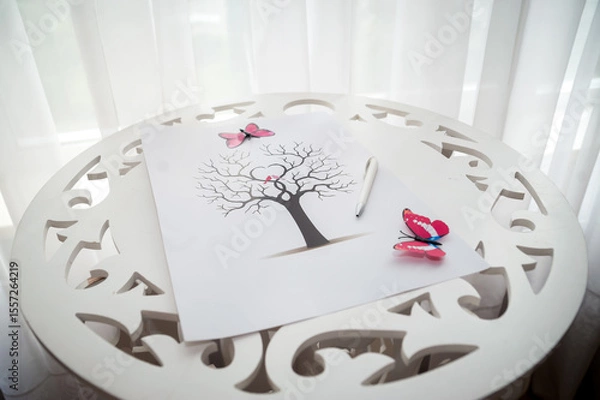 Fototapeta Artistic tree drawing on a table. A detailed tree drawing with butterflies rests on a decorative table by a bright window, highlighting creativity.