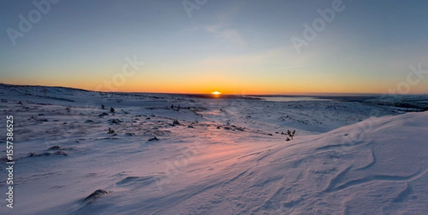 Obraz A breathtaking winter sunrise over a vast, snow-covered mountain plateau. The early morning sun casts a warm golden and pink glow across the untouched landscape.