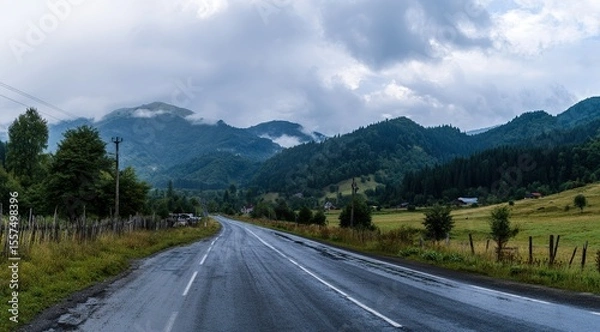Fototapeta The road leads to the mountains, with tree-lined mountain roads, cloud-shrouded mountains in front of and behind, and damp asphalt pavement. Forest after rain with misty mountain background.