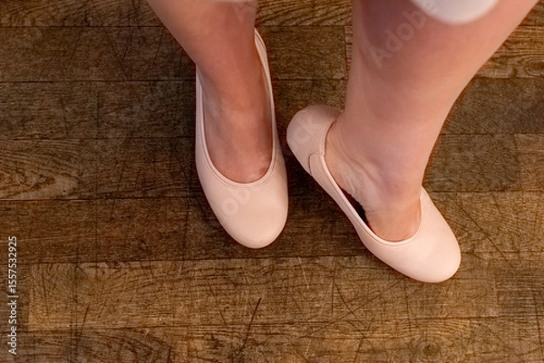 Fototapeta Dancer practices grace and poise in soft ballet shoes on warm wooden floor during a twilight rehearsal