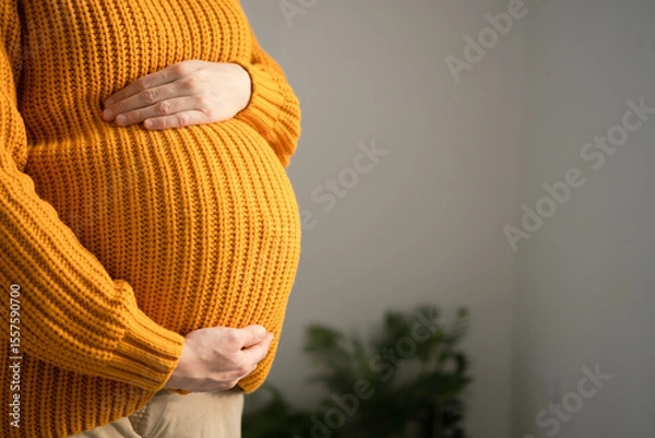 Fototapeta Serene close-up of pregnant woman's hands lovingly touching her baby bump. Heartwarming scene of prenatal connection in cozy home environment.