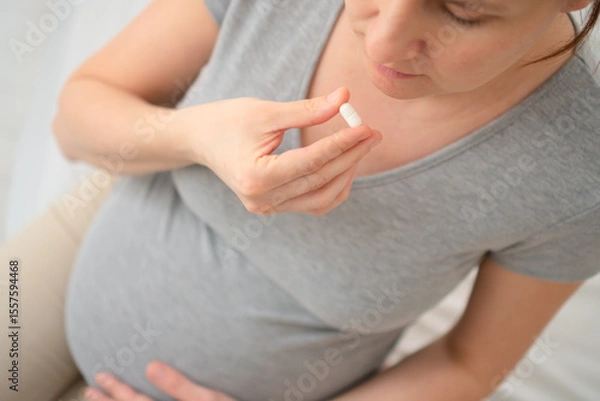 Fototapeta Close-up top view of pregnant woman hand with a pill. Concept of prenatal medication and health monitoring.
