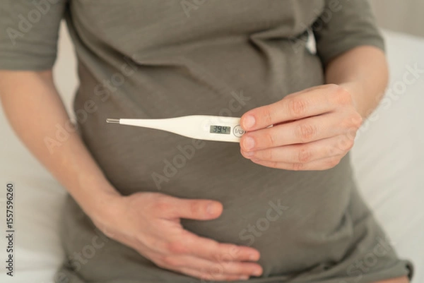 Fototapeta Expecting mother using thermometer while resting at home. Careful health monitoring during pregnancy when feeling under the weather.