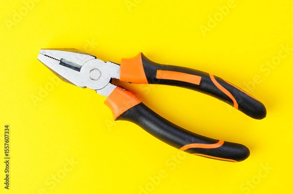 Fototapeta Metal pliers tool with rubber handles on bright yellow background top view